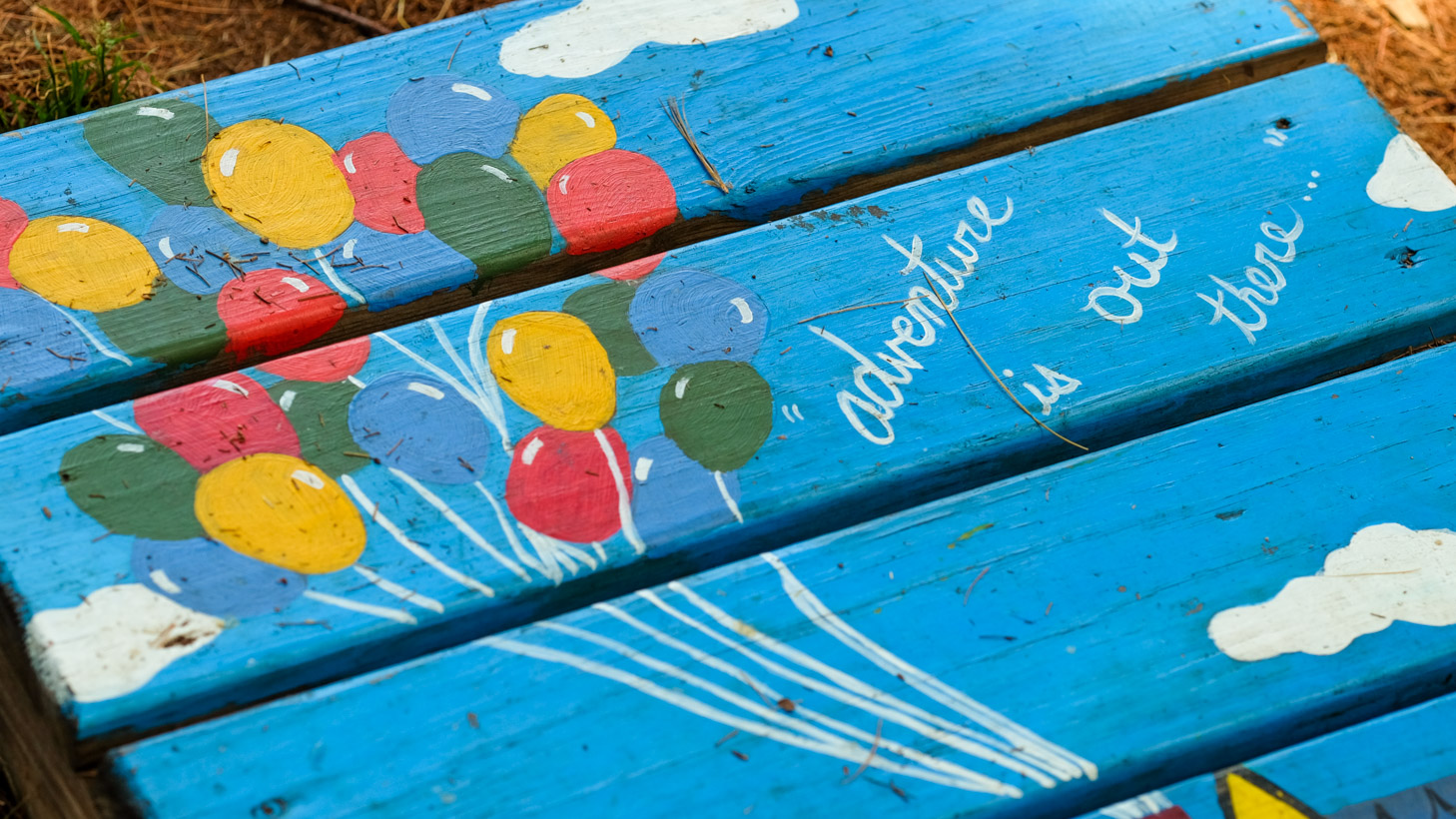 Pallet board painted with a scene of the balloons from the movie Up and the quote "adventure is our there"