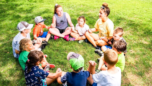 Group of kids and counselors sitting in a circle on the grass