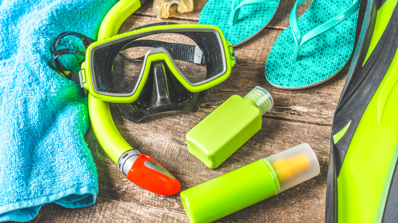 Flat lay of snorkel mask and tube next to flip flops and sunscreen