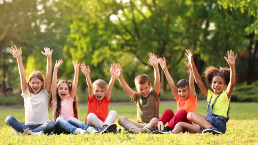 Line of kids sitting in the grass with their hands up in excitement