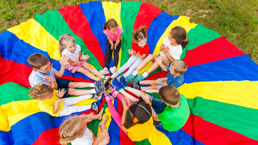 Group of kids sitting in a circle on top of a parachute