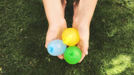 Child holding three different water balloons in their hands.