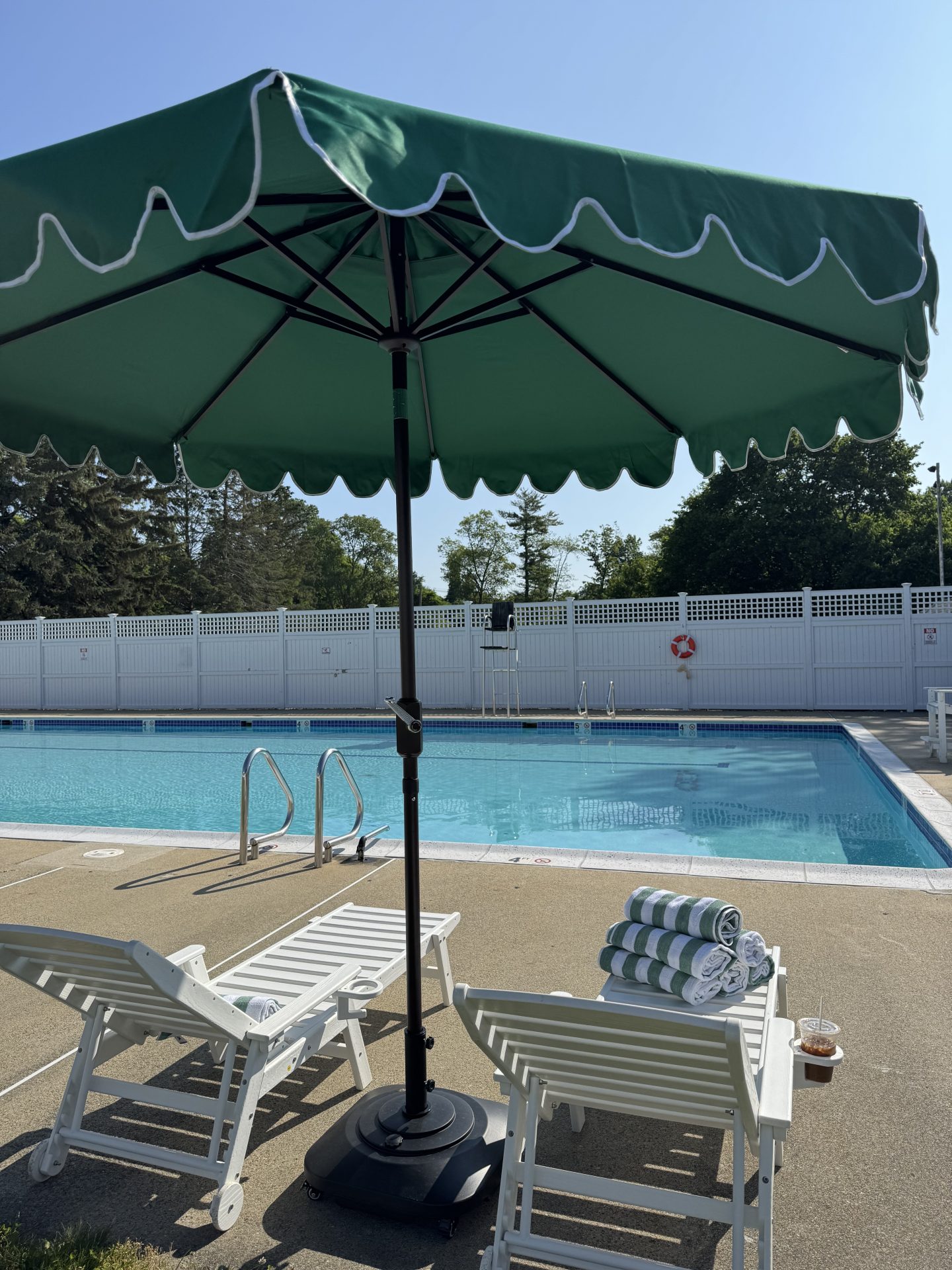 A green umbrella covering two white lounge chairs next to the Summer at Brooks pool