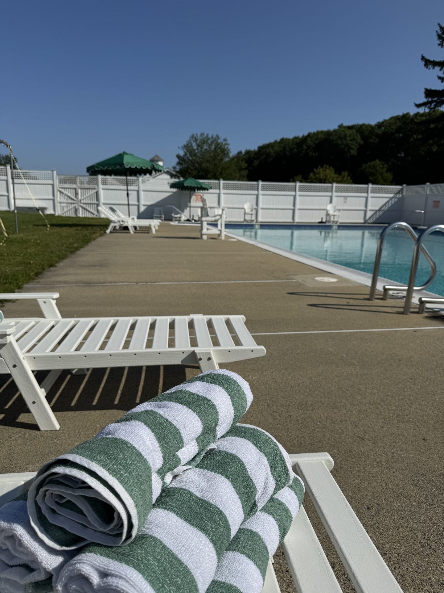A close-up of two white lounge chairs with a stack of green and white towels on one of them